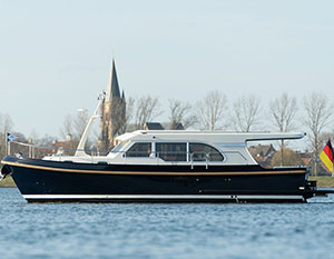 Linssen GS 30 Sedan Amy, Backbordansicht, Fahrt von rechts nach lnka, Ufer und Kirchturm im Hintergrund, zeitiges Frühjahr