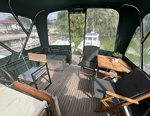 Linssen 30.9 Simba am Anleger. Blick vom Cockpit auf Achterdeck durch geöffnete Tür bei geschlossener Persenning in den Hafen, Hintergrund Boote im Hafen